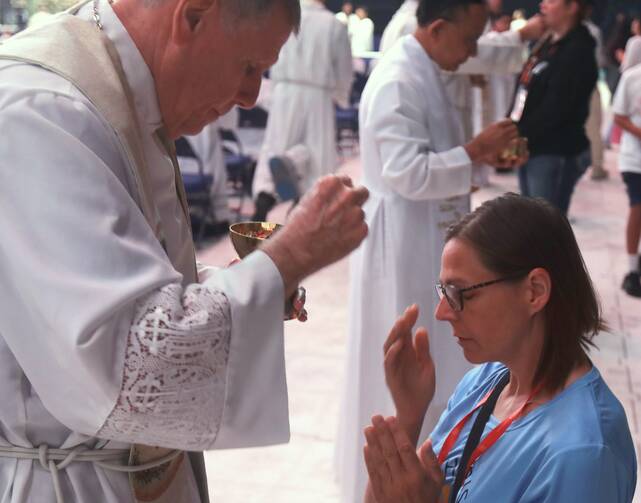 A pilgrim crosses herself after receiving Communion on her knees July 20, 2024, at Lucas Oil Stadium in Indianapolis during the National Eucharistic Congress. (OSV News photo/Bob Roller)