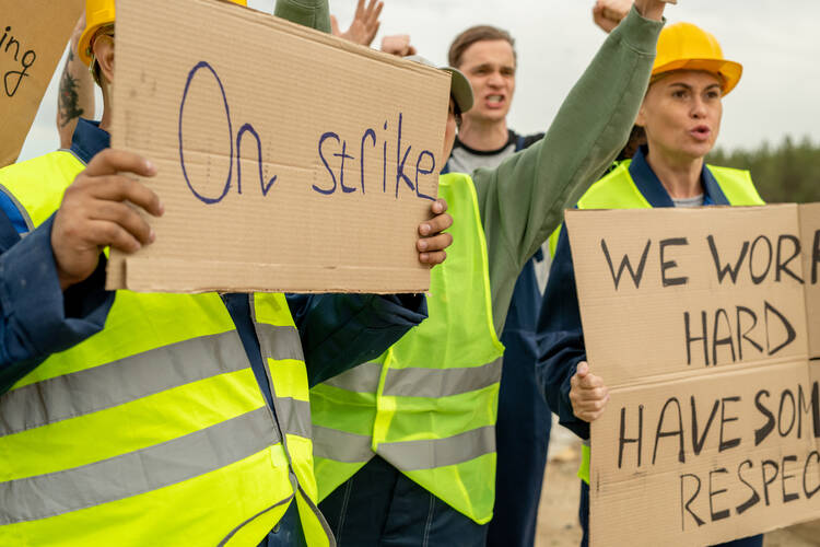 A group of people in yellow vests holding signs saying "On strike" and "We work hard, show some respect"