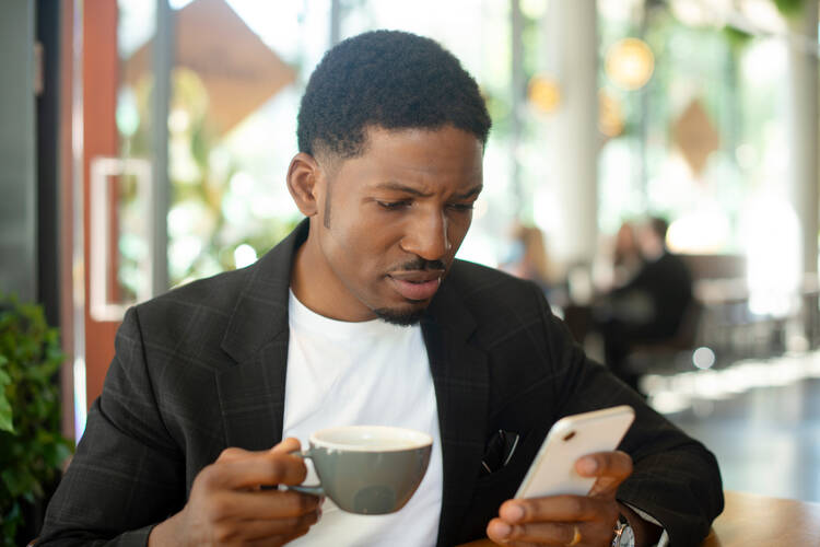 A young man looks with concern at his cellphone in one hand, while holding a cup of coffee in the other. (istock/Tassii)