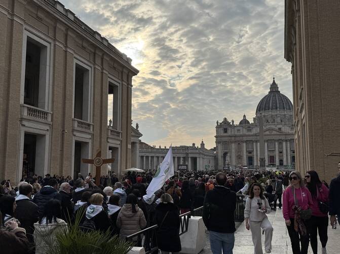 pilgrims make their way toward st peters basilica under a cloudy sky