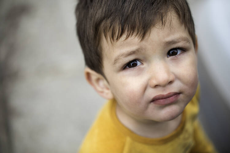 Photo of young boy with dark hair, wearing a yellow T-shirt, looking up at the camera with a sad expression (iStock/123ducu)