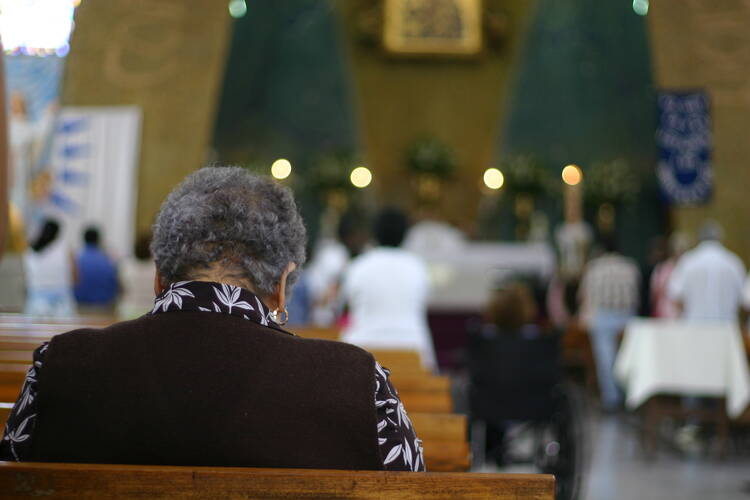 Middle-aged Black woman, seen from behind, sits alone in a pew during Catholic Mass (iStock/abalcazar)