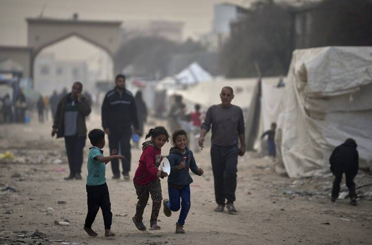 Displaced Palestinian children run past tents at the Islamic University of Gaza compound amid the ongoing war in Gaza, Sunday, April 6, 2025. (AP Photo/Jehad Alshrafi)