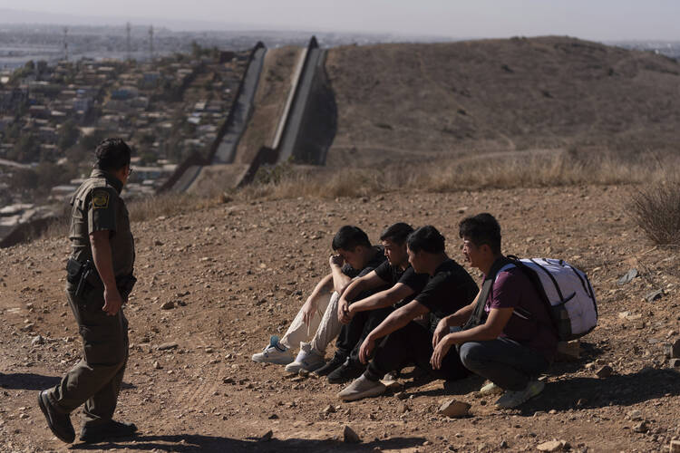 A U.S. Border Patrol agent walks past four men being detained after crossing the border through a gap in the walls separating Mexico and the United States on Jan. 23, 2025, in San Diego. (AP Photo/Gregory Bull, File)