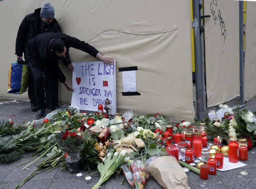 A man attaches a poster "The light is stronger than the darkness" in Berlin, Germany, Tuesday, Dec. 20, 2016, the day after a truck ran into a crowded Christmas market and killed several people. (AP Photo/Matthias Schrader)