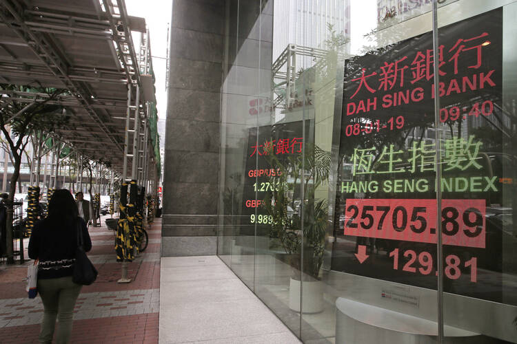 People walk past an electronic board showing Hong Kong share index outside a local bank in Hong Kong Monday, Jan. 8, 2019. (AP Photo/Vincent Yu)