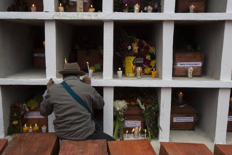 In this Nov. 30, 2017 photo, an Ixil Maya man prays next to the niches where 172 civil war victims were placed, at the cemetery in Santa Avelina, Guatemala. Since the exhumations in Santa Avelina began in 2014, experts have identified 108 of the victims through DNA testing or through personal objects recognized by surviving family members. (AP Photo/Luis Soto)