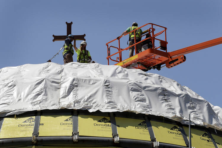 In this Aug. 10, 2017 file photo, construction workers adjust a temporary cross on the St. Nicholas National Shrine in New York. Work on the Greek Orthodox church destroyed in the Sept. 11 attacks next to the World Trade Center memorial plaza has been temporarily suspended by the construction company. It comes amid financial difficulties and questions over how funds have been managed. (AP Photo/Mark Lennihan, File)