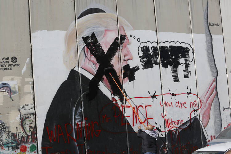 In this Dec. 7, 2017 file photo, a Palestinian defaces a painting on the separation barrier of U.S. President Donald Trump, with a warning that Vice President Mike Pence is not welcome, in Bethlehem, West Bank. Palestinian Christians say Pence's brand of evangelical Christianity, with its fervent embrace of modern-day Israel as fulfilment of biblical prophecy, lacks their faith's compassion and justice, including for those who have endured half a century of Israeli occupation. (AP Photo/Nasser Shiyoukhi, Fi