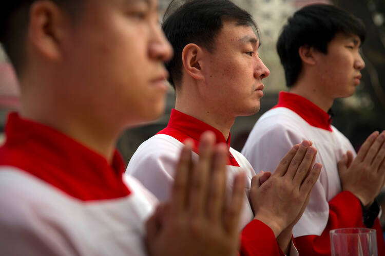 In this March 31, 2018, file photo, Chinese acolytes pray during a Holy Saturday Mass on the evening before Easter at the Cathedral of the Immaculate Conception, a government-sanctioned Catholic church in Beijing. (AP Photo/Mark Schiefelbein, File)