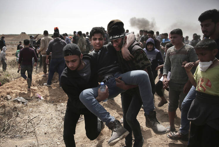 Palestinian protesters evacuate a wounded youth who was shot by Israeli troops during a protest at the Gaza Strip's border with Israel on April 13. Palestinians streamed to tent camps on Gaza's border with Israel for a third mass protest. (AP Photo/ Khalil Hamra)
