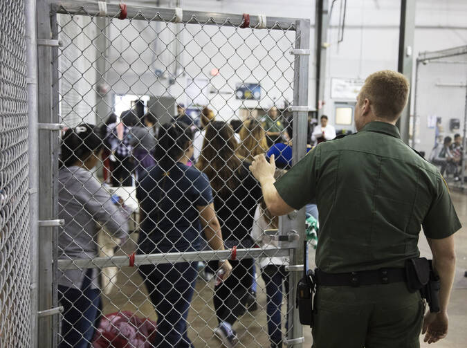 A U.S. Border Patrol agent watches as people who've been taken into custody related to cases of illegal entry into the United States, stand in line at a facility in McAllen, Texas, Sunday, June 17, 2018. (U.S. Customs and Border Protection's Rio Grande Valley Sector via AP)