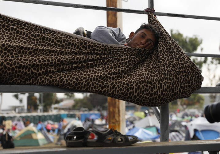 A migrant rests inside a blanket tied to keep him from rolling off the spectator stands at the Benito Juárez Sports Complex in Tijuana, Mexico. (AP Photo/Rebecca Blackwell)