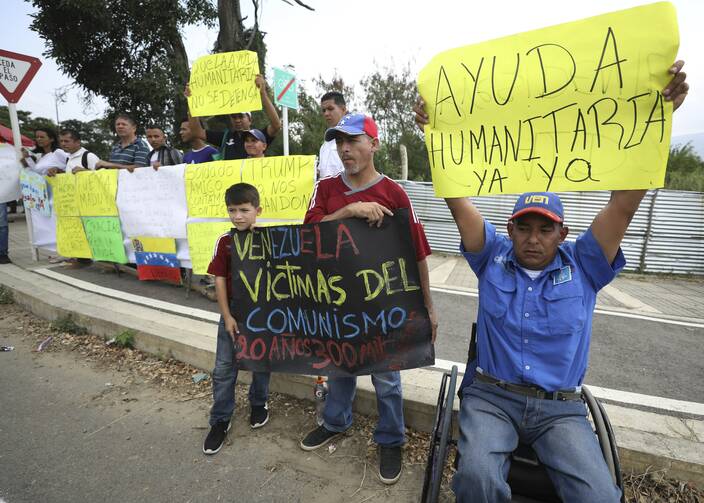 Demonstrators hold signs in support of the country's self-proclaimed president Juan Guaido and and for foreign humanitarian aid, next to the Tienditas International Bridge, near Cucuta, Colombia, on Feb. 8. (AP Photo/Fernando Vergara)