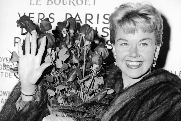In this April 15, 1955, file photo, American actress and singer Doris Day holds a bouquet of roses at Le Bourget Airport in Paris after flying in from London. (AP Photo, File)