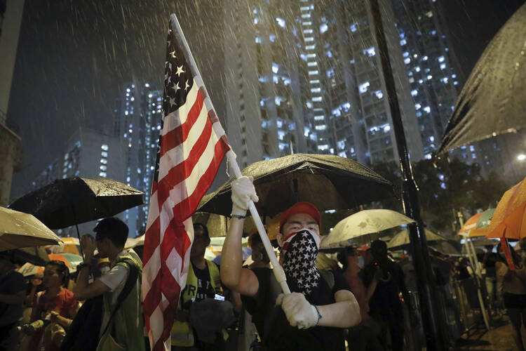 A protester waves a U.S. flag as hundreds of protesters gather outside Kwai Chung police station in Hong Kong on July 30. Protesters clashed with police again in Hong Kong on Tuesday night after reports that some of their detained colleagues would be charged with the relatively serious charge of rioting. (AP Photo/Vincent Yu)