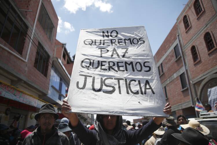 A supporter of former President Evo Morales holds a sign with a handwritten message that reads in Spanish: "We don't want peace, We want justice," during a protest at a blocked highway in El Alto, on the outskirts of La Paz, Bolivia, Wednesday, Nov. 20, 2019. (AP Photo/Natacha Pisarenko)