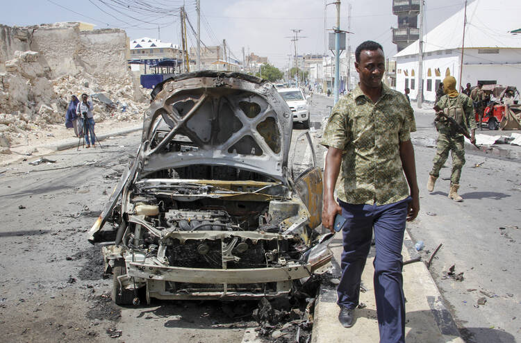 Security forces and others walk past the wreckage of vehicles after a vehicle bomb attack on a security checkpoint located near the presidential palace, in Mogadishu, Somalia, Wednesday, Jan. 8, 2020. (AP Photo/Farah Abdi Warsameh)