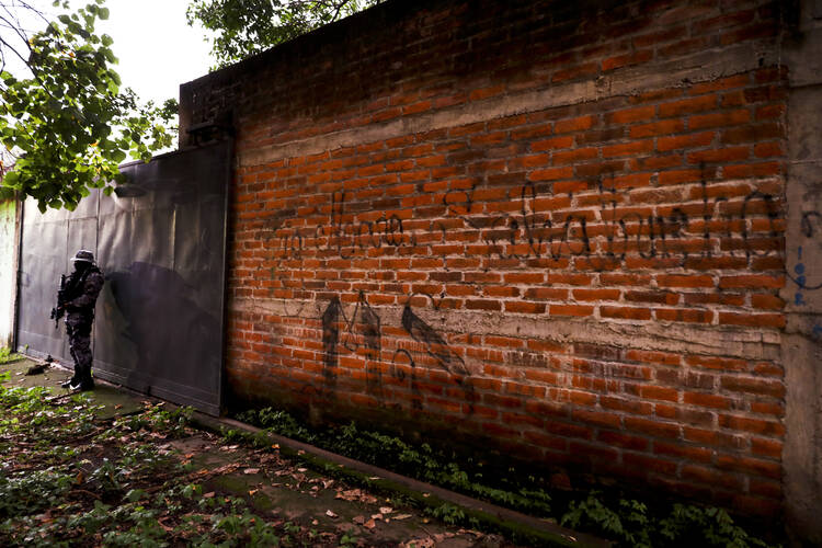 In this Oct. 10, 2019, file photo police guard next to a graffiti wall with the name of a gang as part of a routine patrol in Lourdes, La Libertad, El Salvador. The Human Rights Watch in the report being released Wednesday, Feb. 5, 2020, said that at least 138 people deported to El Salvador from the U.S. in recent years were subsequently killed. The new report comes as the Trump administration makes it harder for Central Americans to seek refuge here. (AP Photo/Eduardo Verdugo, File)