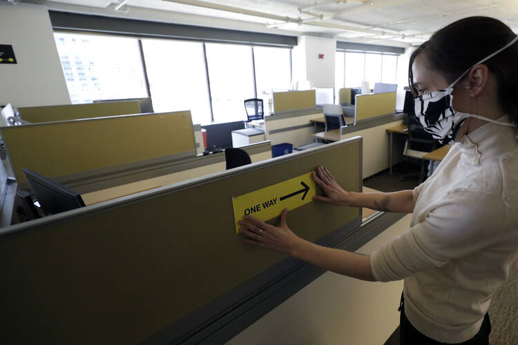Stephanie Jones posts a sign mandating one-way foot traffic among the cubicles at the design firm Bergmeyer, in Boston, in response to the coronavirus pandemic. (AP Photo/Steven Senne)