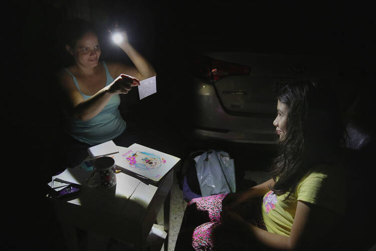Margarita Rodriguez holds a flashlight as she quizzes her 11-year-old daughter Isel Martinez on homework outside their home in San Juan, Puerto Rico, Oct. 25. Most of Puerto Rico has been without power and water for more than one month after Hurricane Maria devastated the island (CNS photo/Bob Roller).