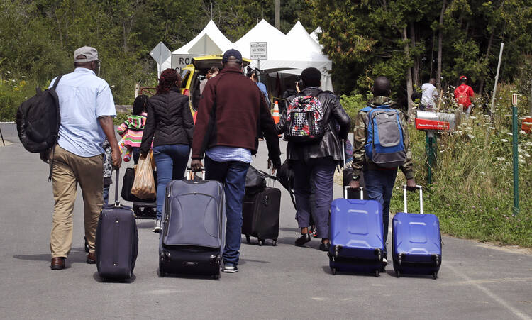 A family from Haiti approach a tent in Saint-Bernard-de-Lacolle, Quebec, stationed by Royal Canadian Mounted Police, as they haul their luggage down Roxham Road in Champlain, N.Y., Monday, Aug. 7, 2017. (AP Photo/Charles Krupa)