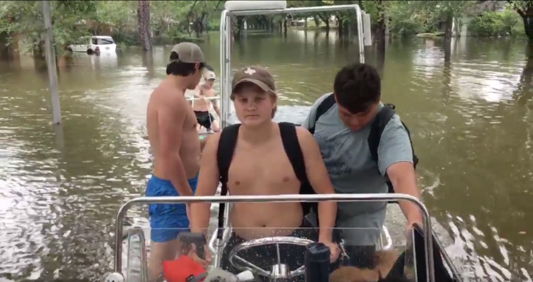 Declan Conner, center, steers his family's fishing boat through their flooded neighborhood outside Houston Aug. 27. (Screenshot via Mark Mulligan on Twitter)