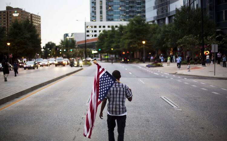 Skylar Barrett walks with an American flag in the middle of the street during a march through the Buckhead neighborhood against the recent police shootings of African-Americans on Monday, July 11, 2016, in Atlanta. (AP Photo/David Goldman)