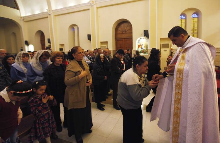 A priest gives Communion during Mass at a church in Baghdad March 1. Christian organizations have begun funneling aid to Syrian cities that are housing refugees from the Islamic State. (CNS photo/Ahmed Saad, Reuters)