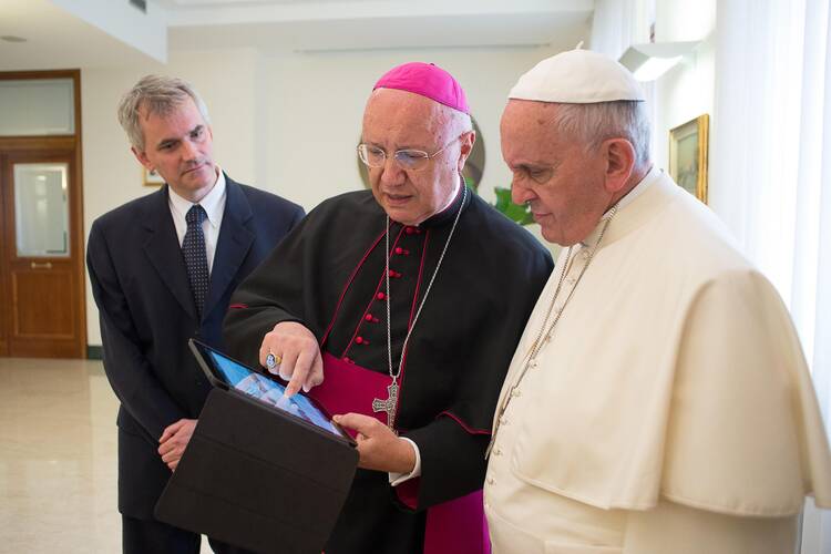 Archbishop Claudio Celli, president of the Pontifical Council for Social Communications, center, shows Pope Francis news on a tablet during a meeting at the Vatican on July 7.