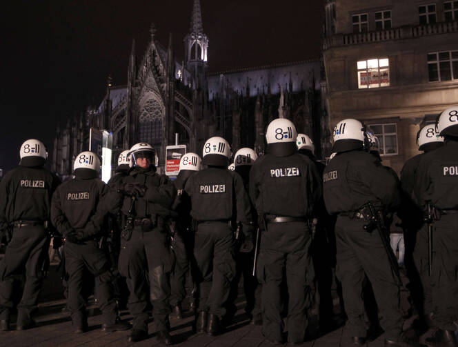 An anti-racism poster is displayed in a window of a building Jan. 21 as police stand guard in front of the cathedral in Cologne, Germany. (CNS photo/Ina Fassbender, Reuters) 