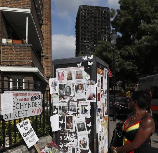 A woman looks towards missing posters stuck on a phone box in front of the remains of Grenfell Tower in London on June 17, 2017. ﻿﻿Police say it will take weeks or longer to recover and identify all the dead in the public housing block fire. (AP Photo/Kirsty Wigglesworth)