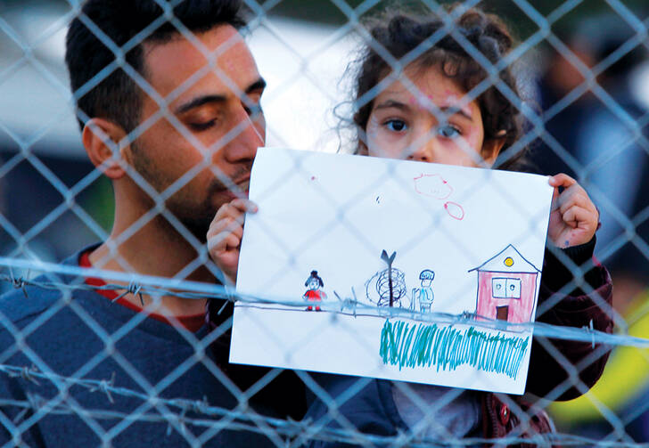 FENCED IN. A young refugee girl holds up a drawing in a makeshift camp on the Macedonian-Greek border, November 2015. 