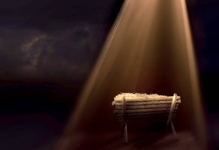 In a dark room, a wooden manger sits in a beam of light pouring through a window