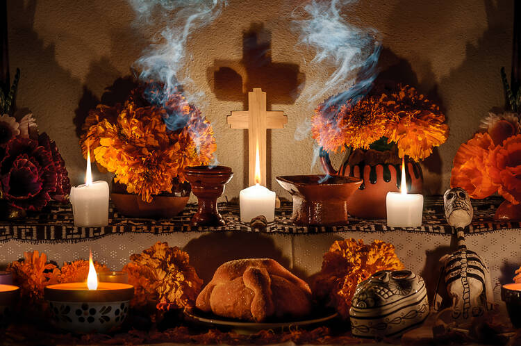 small altar with orange flowers around with cross and smoke in the middle, some dia de los muertos items on the altar in front of the cross
