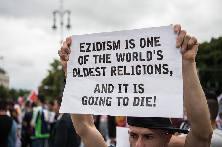 A participant of a rememberance march of Yazidis for the attack on the religious and ethical minorities in North Iraq by the Islamic State in 2014 holds a poster in Berlin, Germany, Wednesday, Aug. 3, 2016. (Wolfram Kastl/dpa via AP)