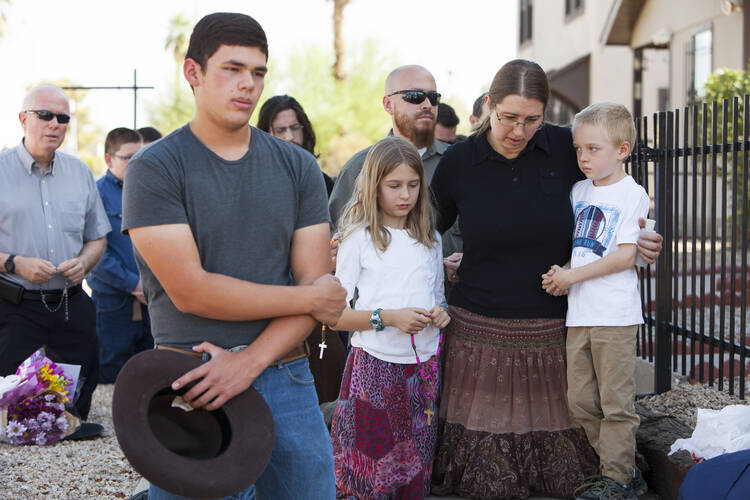 Parishioners, including Jennifer Gustke, right, with her children, pray the rosary near Mater Misericordiae (Mother of Mercy) Mission in Phoenix the morning after a priest was killed and another critically injured during an attack at the mission's rectory