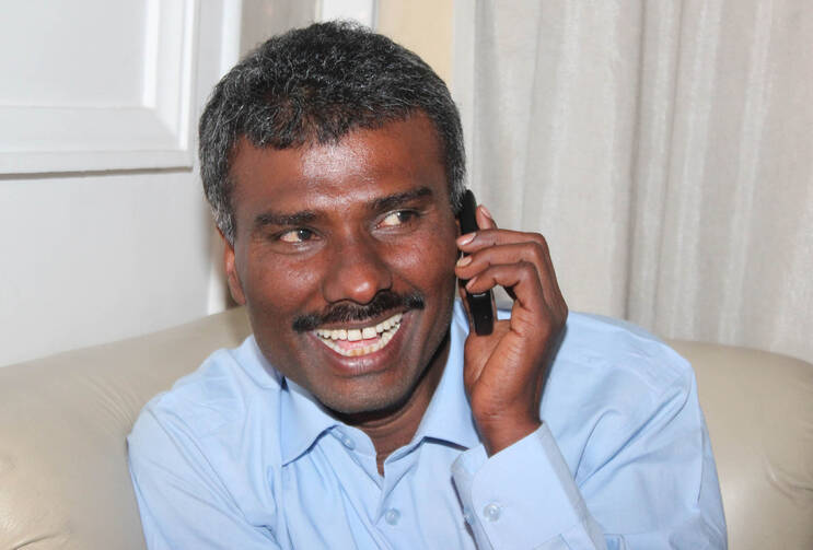 Jesuit Father Alexis Prem Kumar, who was kidnapped in Afghanistan and was held for more than eight months, speaks on a cell phone on his arrival in New Delhi Feb. 22. (CNS photo/Anto Akkara)