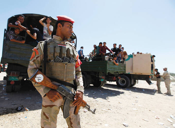 ON GAURD. An Iraqi soldier stands before truckloads of volunteers in Baghdad on June 17, eager to fight Sunni militants converging on the city. 