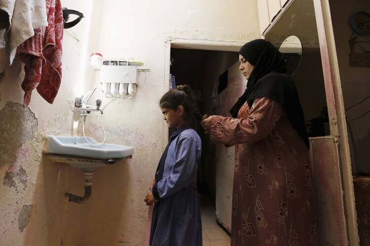 Rana, a 31-year-old a Syrian refugee living in Jordan, adjusts her 8-year-old daughter's hair at their home at a refugee camp in Amman. World Refugee Day is June 20.