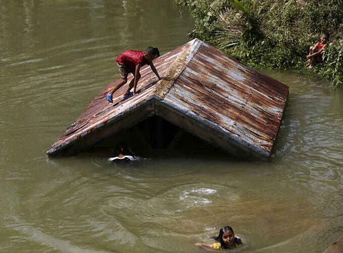 Children swim in a swollen river on Samar Island, Philippines, Dec. 8. Typhoon Hagupit left at least 21 people dead and forced more than a million people into shelters (CNS photo/Francis R. Malasig, EPA).