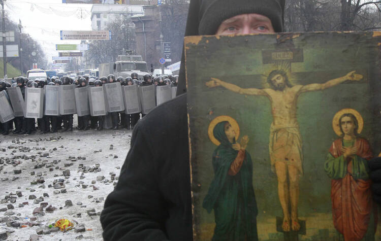 A priest stands between police and protestors in Kiev.