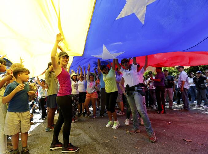 Opposition members wave a Venezuelan flag outside a poll station during a symbolic referendum in Caracas, Venezuela, on July 16. Venezuela's opposition called for a massive turnout Sunday in a symbolic rejection of President Nicolas Maduro's plan to rewrite the constitution, a proposal that's escalating tensions in a nation stricken by widespread shortages and more than 100 days of anti-government protests. (AP Photo/Ariana Cubillos)