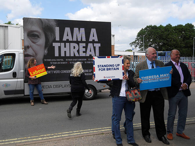 Labour Party supporters, rear, stand next to an electronic billboard behind Conservative Party supporters, front, outside a campaign event attended by Britain's Prime Minister Theresa May in Norwich, Britain, on June 7, 2017. Photo courtesy of Reuters/Toby Melville