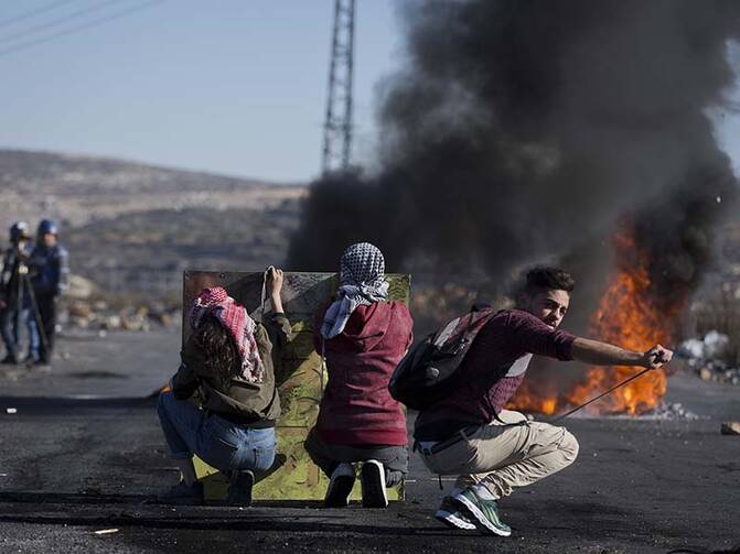 Palestinian protesters take cover behind a metal plate during clashes with Israeli troops following protests against U.S. President Donald Trump’s decision to recognize Jerusalem as the capital of Israel, in the West Bank city of Ramallah on Friday, Dec. 8, 2017. (AP Photo/Nasser Nasser)