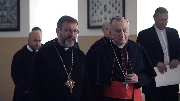 Two Catholic priests sit side by side wearing black clerical robes