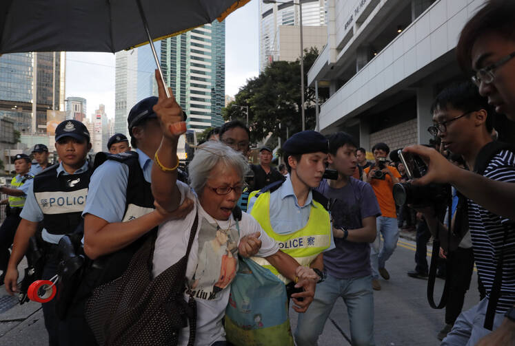 A protester is taken away by police officers as a prison bus carrying Hong Kong activist Joshua Wong leaves the high court after his sentencing in Hong Kong on Aug. 17. A court overturned sentences that the prosecution said were too light and sent Wong and two other student leaders of huge pro-democracy protests in 2014 to prison. (AP Photo/Vincent Yu)