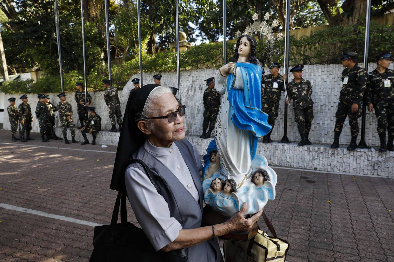 A nun holds a statue of Mary Feb. 23 as soldiers prepare for a flag-raising rehearsal for ceremonies marking the February 1986 anniversary of the People Power Revolution in Manila, Philippines. The nonviolent revolution led to the toppling of President Ferdinand Marcos and the restoration of the country's democracy. (CNS photo/Rolex Dela Pena, EPA)