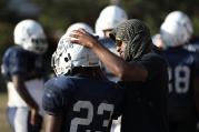 Coach adjusts chin strap on player's football helmet during practice at Maryland Catholic high school.