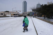 A woman wrapped in a blanket crosses the street near downtown Dallas, Tuesday, Feb. 16, 2021. Temperatures dropped into the single digits as snow shut down air travel and grocery stores. (AP Photo/LM Otero)